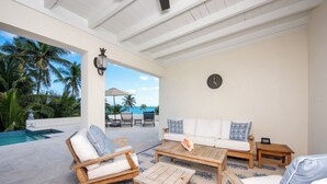Un patio intérieur baigné de lumière, avec une piscine, un canapé blanc, des chaises en bois et une table basse en bois.