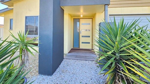 A modern house with a grey pillar, a yellow door, and a wooden deck.
