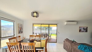 A dining area with wooden chairs and a table, a sofa, and a view of the outdoors through a sliding door.