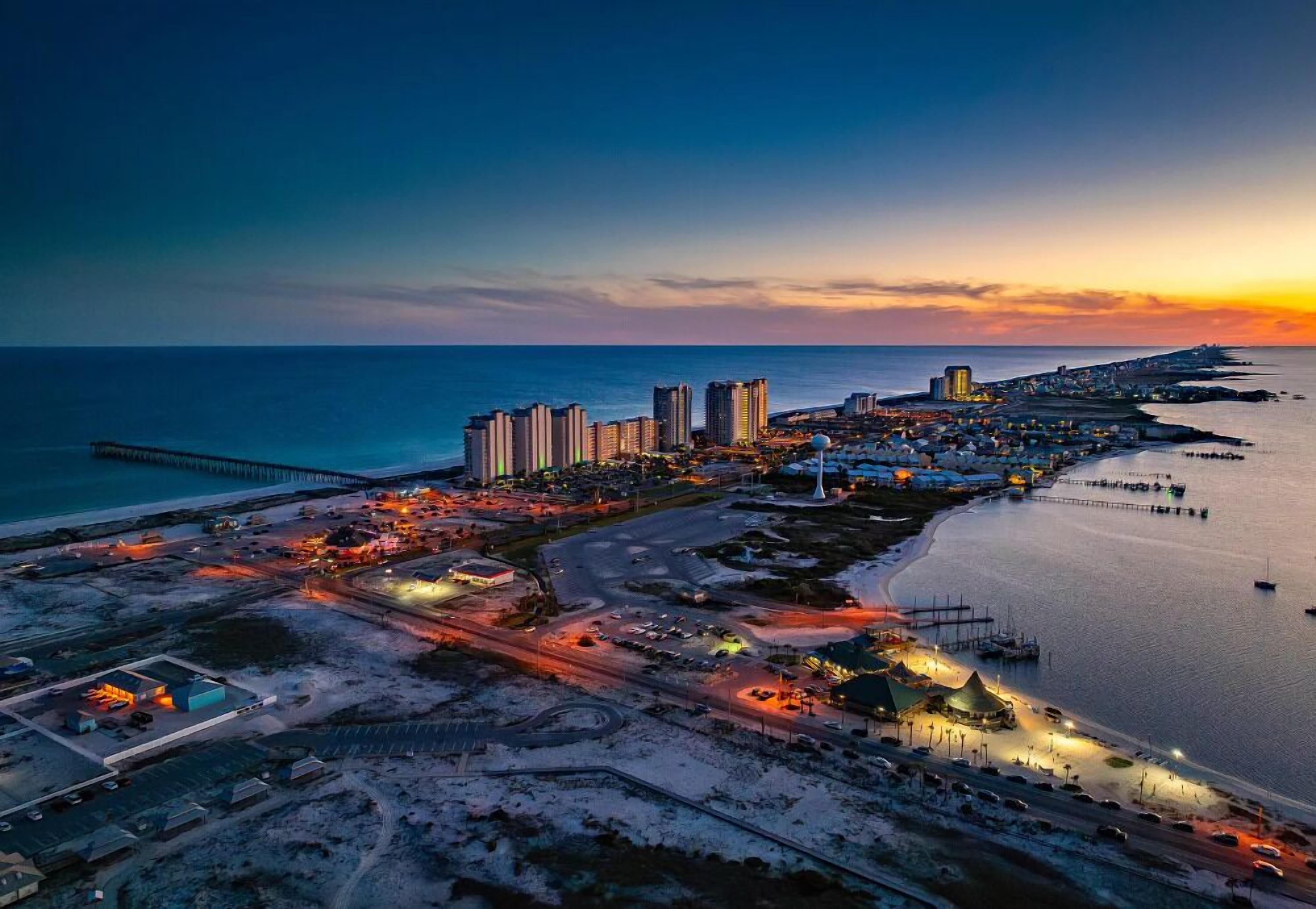 Vista aèria d'una ciutat costanera amb edificis alts, un port esportiu i un llarg moll que s'estén sobre l'aigua.