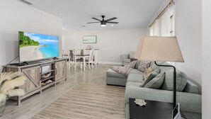 Un salon moderne doté d’un téléviseur à écran plat, d’un ventilateur de plafond, d’un canapé, d’une table basse et d’un coin repas avec une table et des chaises.