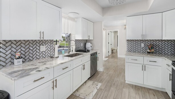 Une cuisine moderne avec des meubles blancs, un plan de travail en marbre et un dosseret en carreaux disposés en motif chevron.