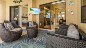 Un espace extérieur aménagé, abrité et doté de mobilier en osier, avec une grande porte vitrée donnant sur le salon.
