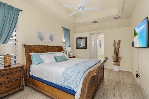 A bedroom with a wooden bed, a ceiling fan, a TV, and a view of the outdoors.
