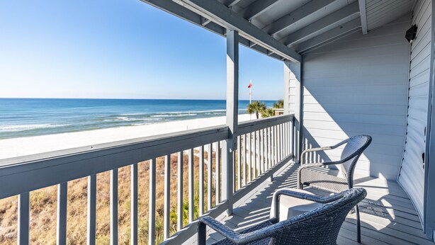 A covered porch with two wicker chairs, a view of the beach, and a flag in the distance. - Luxury Beach Front Townhouse – 4BR/3.5 BA Slps 14! (Panama City Beach)