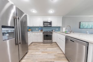 Features stainless steel appliances, white cabinetry, and a tiled backsplash.