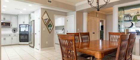 A spacious kitchen with white cabinets, a large wooden dining table, and a chandelier.
