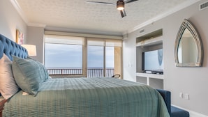 Une chambre avec un grand lit, un ventilateur de plafond, une télévision et une vue sur l’océan.