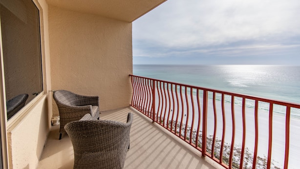 Un balcon avec des fauteuils en osier, une rambarde rouge et une vue sur l’océan.