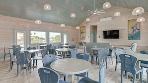 A spacious indoor dining area with multiple tables and chairs, ceiling fans, and a mounted TV. - 8 Sailfish RV Resort, Port Aransas RV Getaway (Port Aransas)