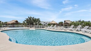 A swimming pool with lounge chairs, palm trees, and thatched-roof structures. - 8 Sailfish RV Resort, Port Aransas RV Getaway (Port Aransas)