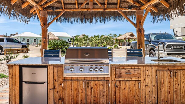 An outdoor grill station with a wooden structure, a refrigerator, and a vehicle in the background. - 8 Sailfish RV Resort, Port Aransas RV Getaway (Port Aransas)