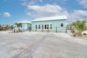 A light blue building with a white roof, a concrete driveway, and palm trees.