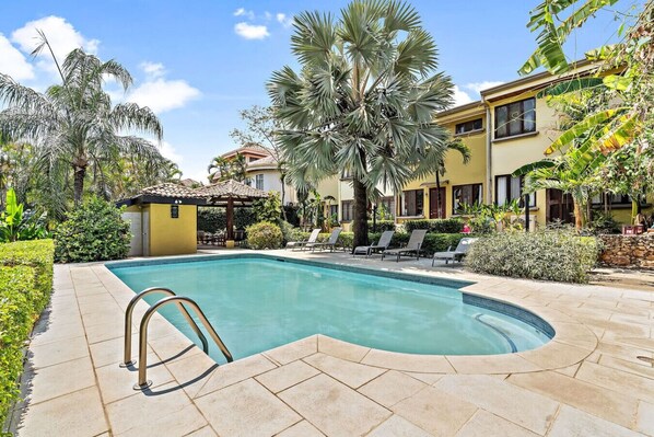 A swimming pool with a curved edge, surrounded by lounge chairs and palm trees.