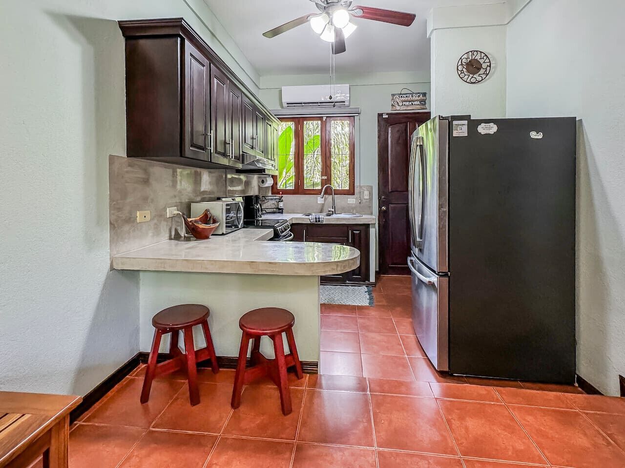 Una cucina con isola centrale, due sgabelli, un frigorifero e una ventola a soffitto.