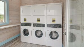 A laundry room with three stacked washing machines and two dryers, wooden walls, and a window. - 36 Sailfish RV Resort, Port Aransas RV Getaway (Port Aransas)