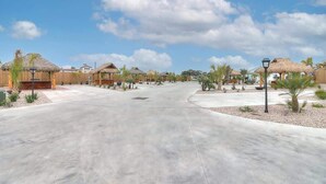 A resort with thatched-roof structures, a paved central area, and palm trees. - 36 Sailfish RV Resort, Port Aransas RV Getaway (Port Aransas)