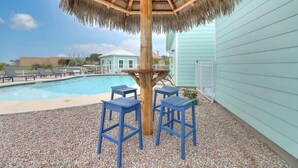A pool area with a thatched umbrella, a table, and four blue chairs. - 36 Sailfish RV Resort, Port Aransas RV Getaway (Port Aransas)
