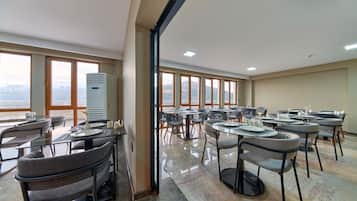 Un'ampia sala da pranzo con diversi tavoli e sedie, grandi finestre con vista sulla città e un moderno condizionatore.
