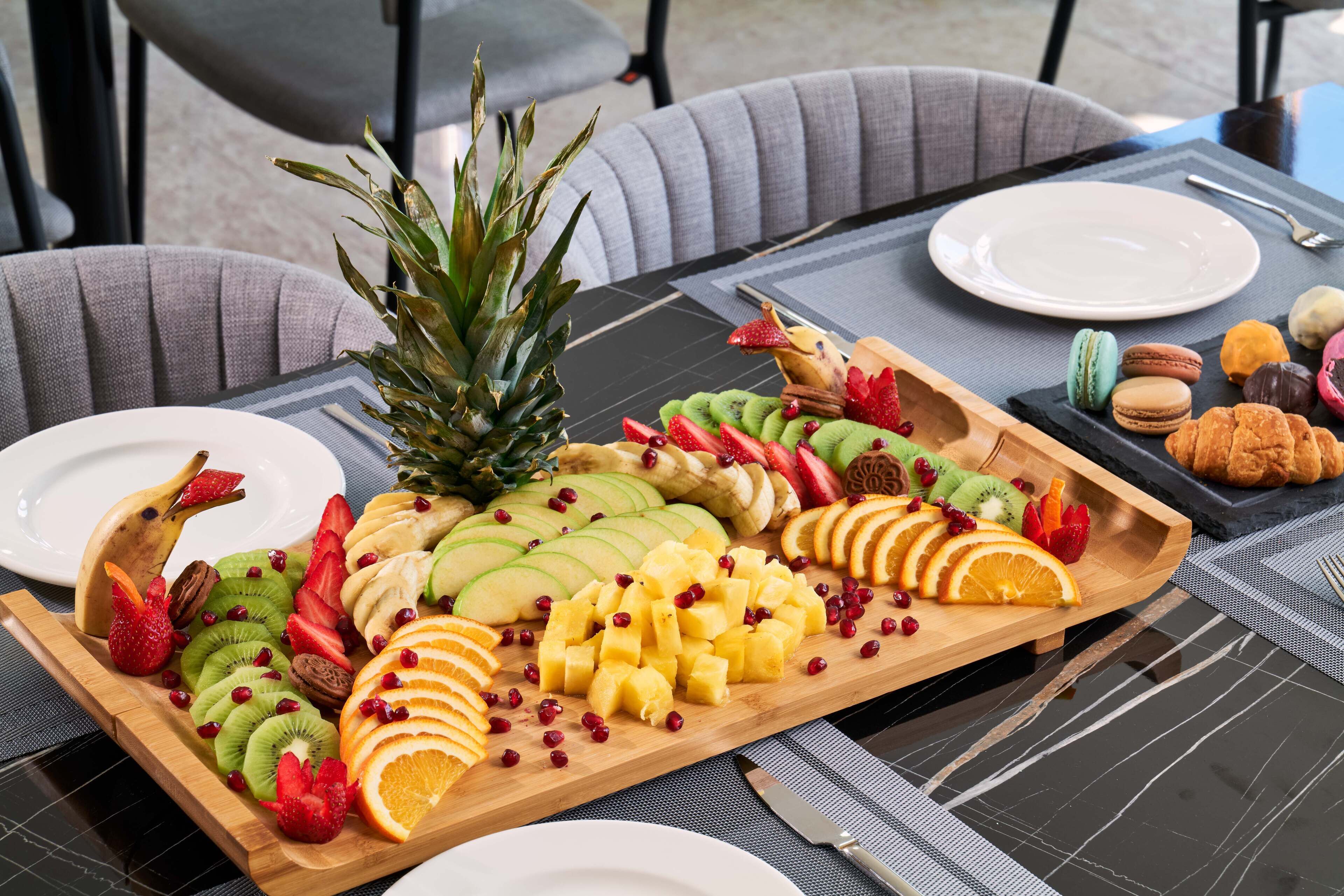 Una mesa servida con una bandeja de frutas, una piña y un plato de pasteles.