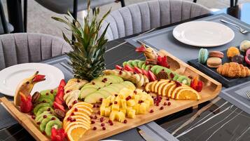 Una mesa servida con una bandeja de frutas, una piña y un plato de pasteles.