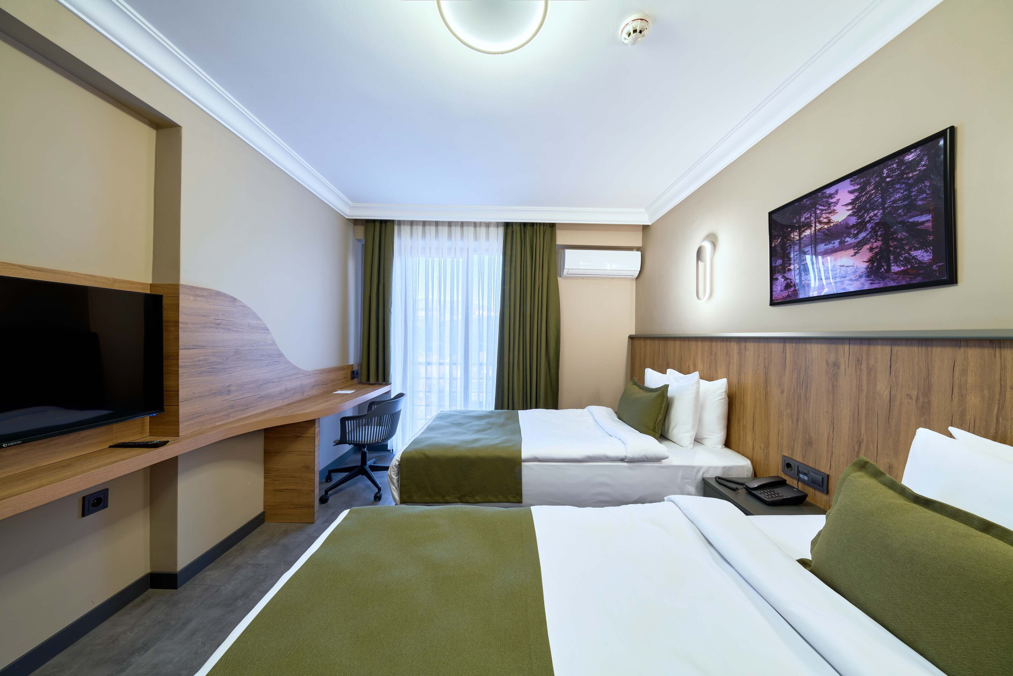 Habitació d'hotel amb dos llits, una taula de treball amb televisió, una cadira i un quadre penjat a la paret.