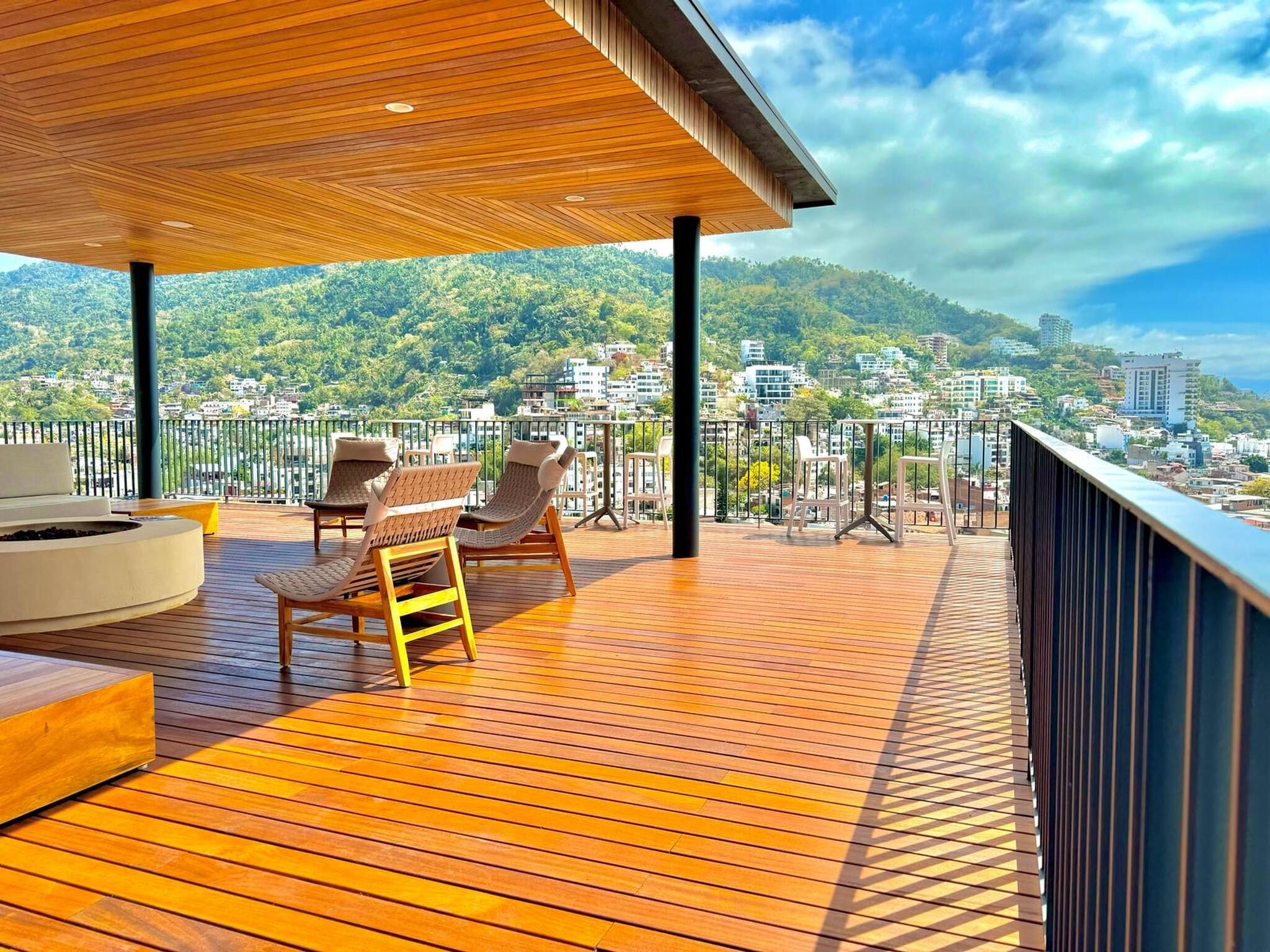 Een houten terras met zitplaatsen en uitzicht op een stadsgezicht.
