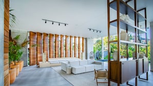 A modern living room with a sectional sofa, wooden slats, and a large window offering a view of greenery.