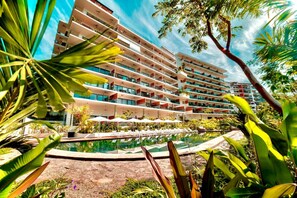 Un hotel de varios pisos con piscina y abundante vegetación.