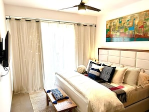 A hotel room with a bed, a bench, a painting, and a ceiling fan.