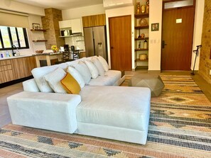 Una sala moderna con un sofá, una cocina al fondo y una alfombra estampada.