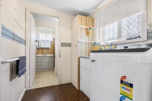 A compact kitchen with a refrigerator, a window with lace curtains, and a door leading to another room. - Beach Comber in Hat Head (Hat Head)