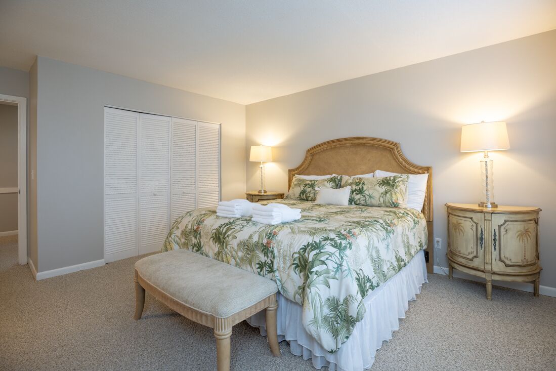A bedroom with a bed, two bedside lamps, a bench, a wardrobe, and a nightstand.