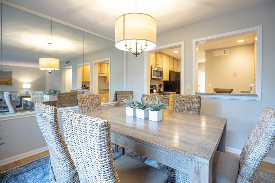 A dining area with a large wooden table, wicker chairs, and a chandelier.