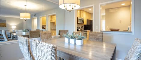 A dining area with a large wooden table, wicker chairs, and a chandelier.