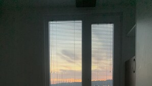 A hotel room with a bed, two windows with blinds, and a view of a bridge and water at sunset. - OLIVA HOUSE BOAT - Unique Experience near Beaches, Amenities, Fun and History (Pula)
