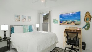 Un dormitorio con cama, mesitas de noche, un escritorio con silla, un ventanal grande y decoración en la pared.