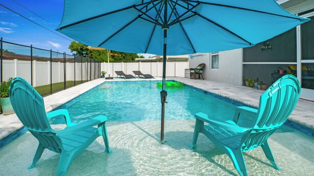 Ein Swimmingpool mit zwei türkisfarbenen Liegestühlen und einem blauen Sonnenschirm.