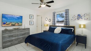Ein Schlafzimmer mit Bett, Kommode, Deckenventilator, Fernseher und Bildern an den Wänden.