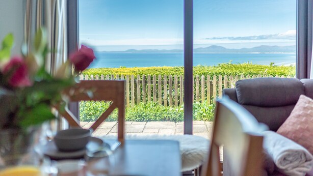 Una stanza con vista sul mare, una recinzione in legno e un tavolo da pranzo con un vaso di fiori.