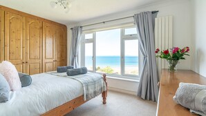 Una camera da letto con un letto, un armadio in legno, una finestra vista mare e un vaso con fiori su un tavolo di legno.
