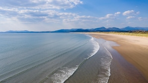 Una spiaggia con vista libera sull'oceano e montagne lontane, sotto un cielo parzialmente nuvoloso.