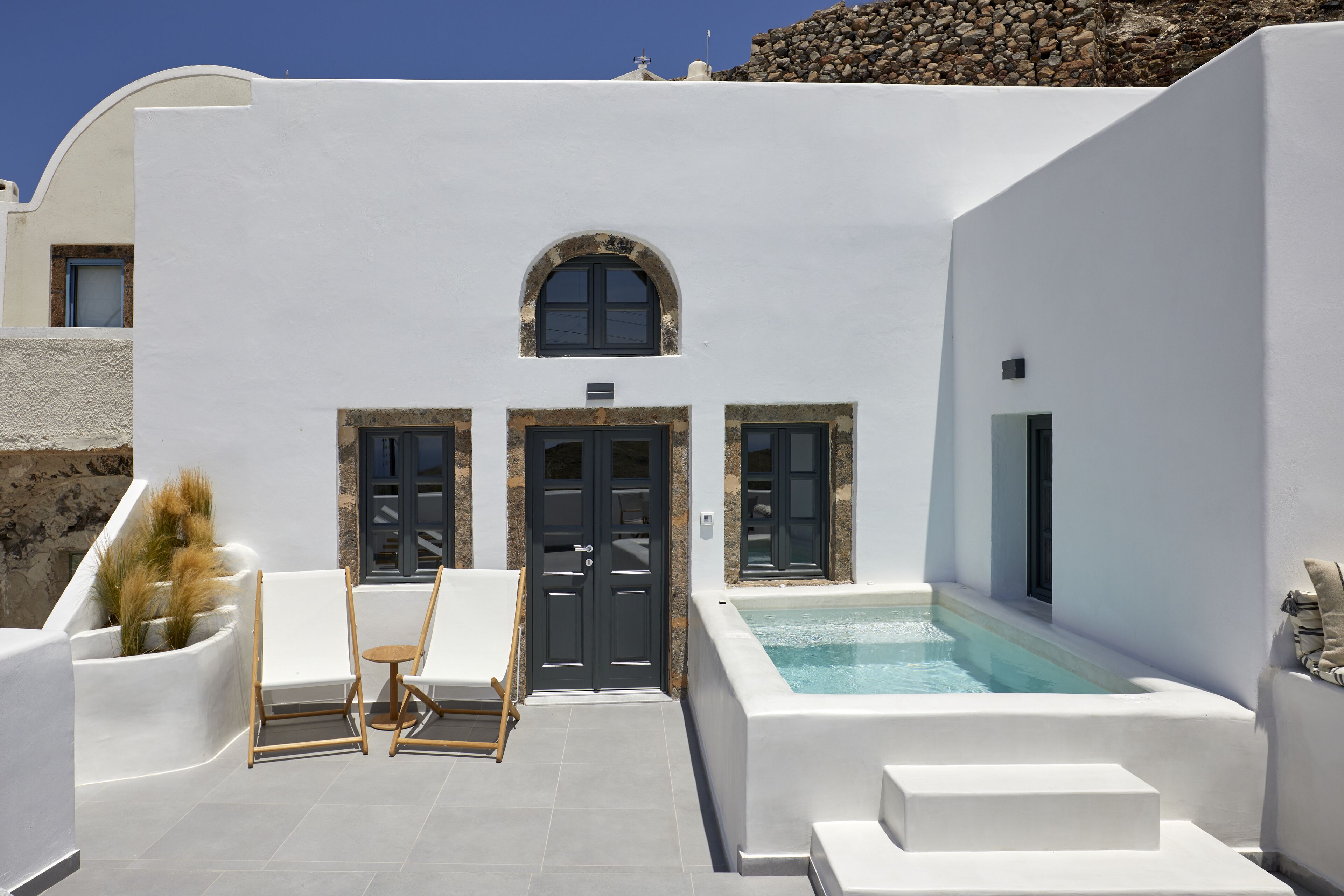 A white-walled building with a pool, two doors, and a small table with chairs.