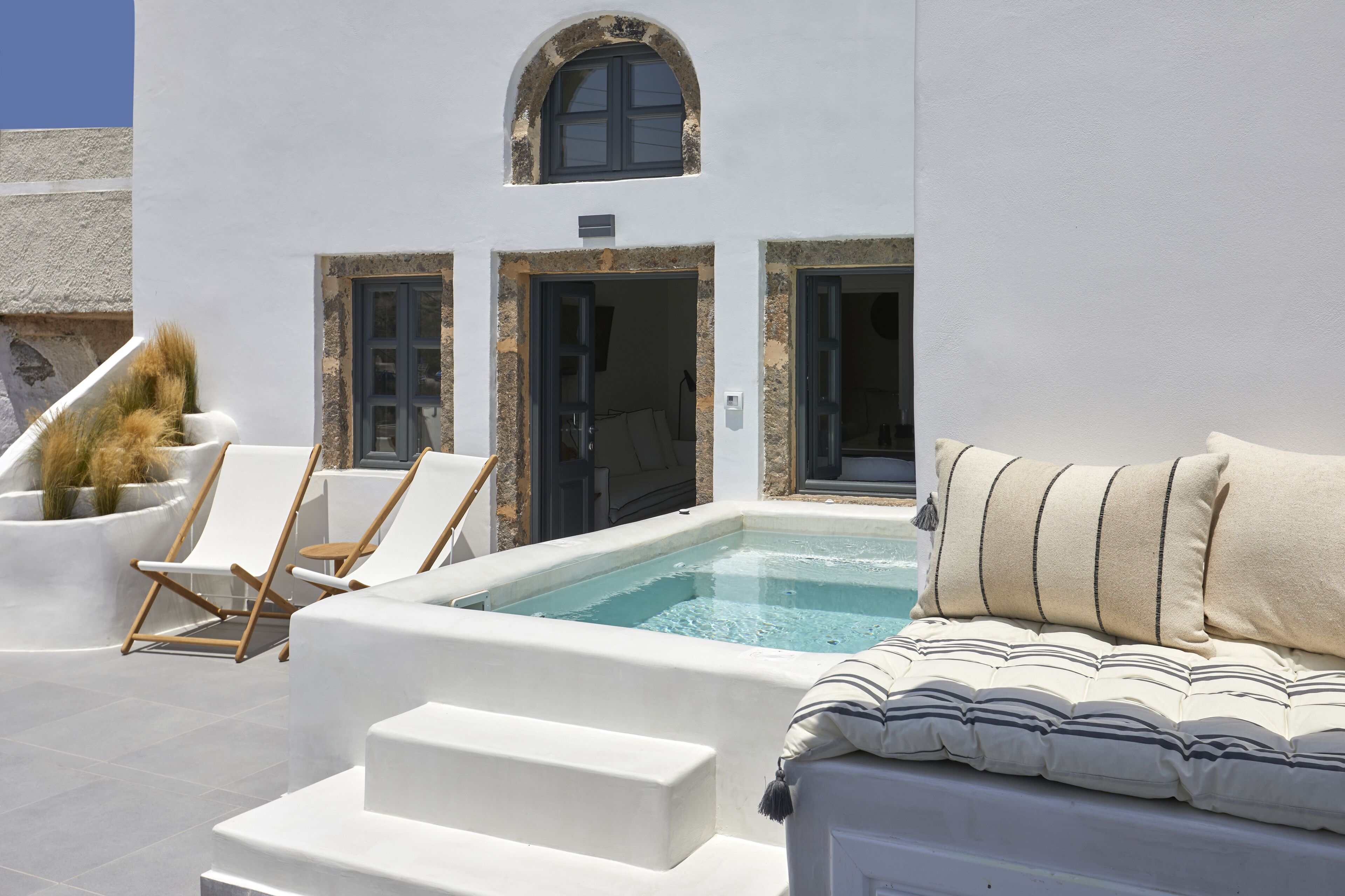 A rooftop pool area with a hot tub, lounge chairs, and a sofa with cushions.