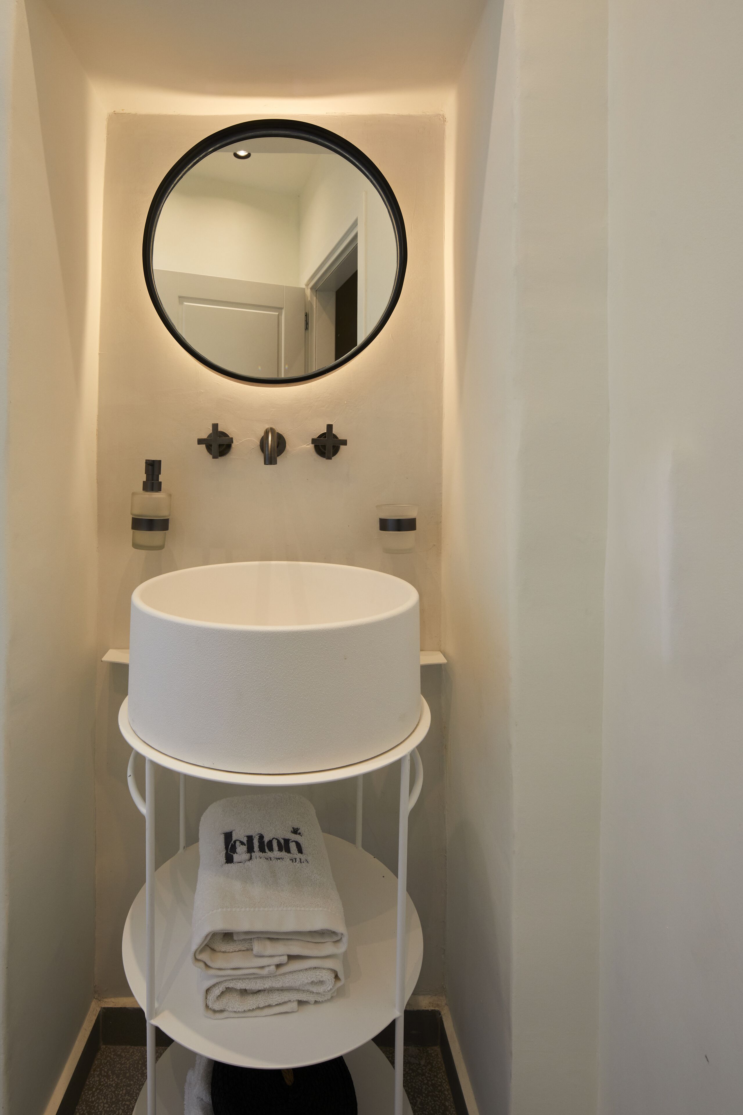 A bathroom with a round mirror, a white sink, and a towel rack with folded towels.