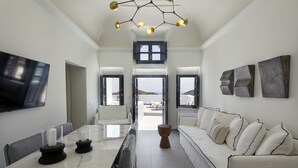 A modern hotel room with a marble dining table, white sofa, and a large window offering a view of the sea. - Lerion Luxury Villas (Santorini)