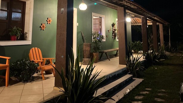 A house with a tiled roof, a porch with a bench, and potted plants.