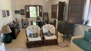 A living room with two upholstered chairs, a sofa, a coffee table, and a dining area with a cabinet and a window with shutters.
