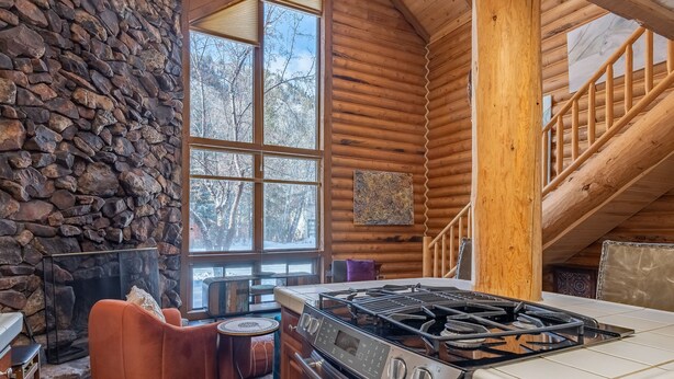 L’intérieur d’une cabane en rondins, avec un mur en pierre, une cheminée, un coin repas et une cuisine équipée d’une cuisinière à gaz.