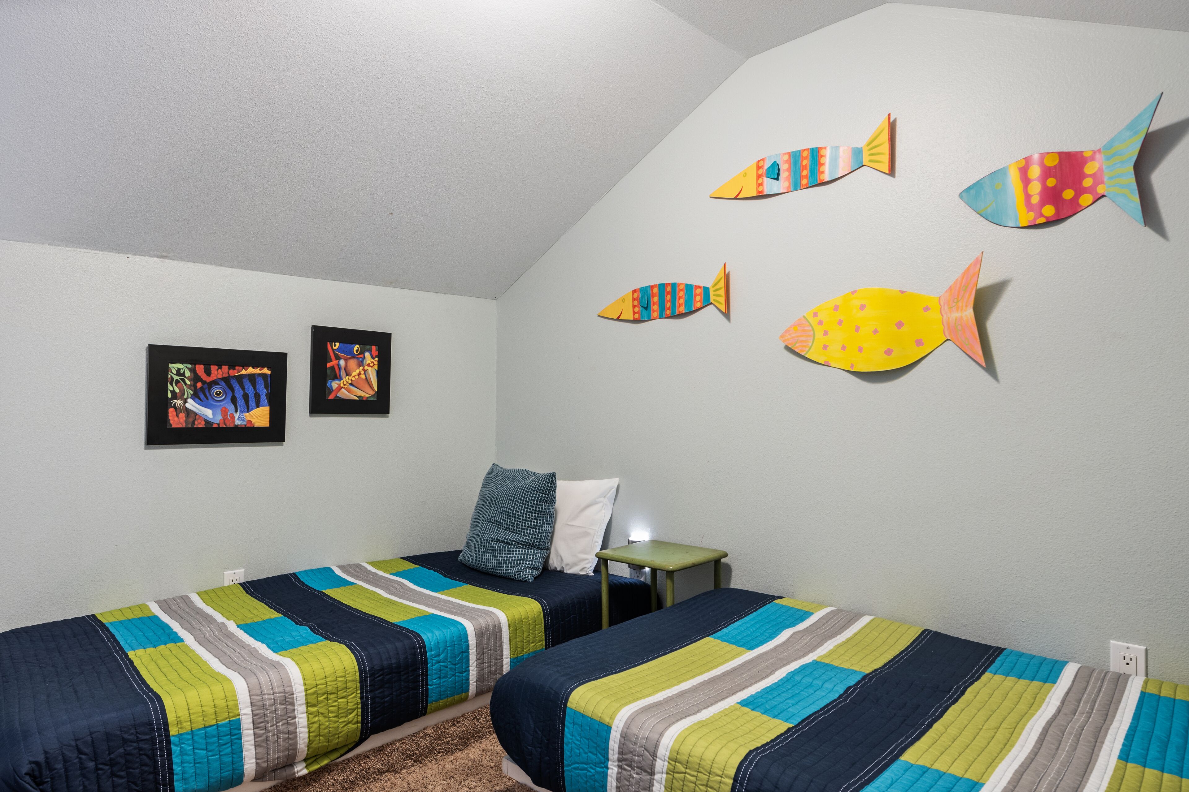 A bedroom with two beds, a nightstand, and wall decorations including fish and framed pictures.